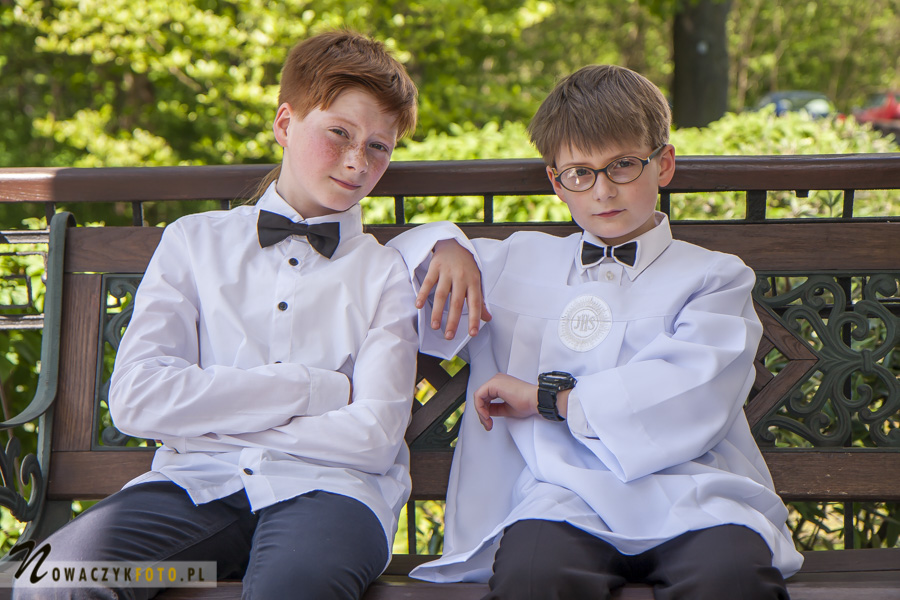 Zdjęcie dwóch chłopców w strojach komunijnych siedzących na ławce pod kościołem
